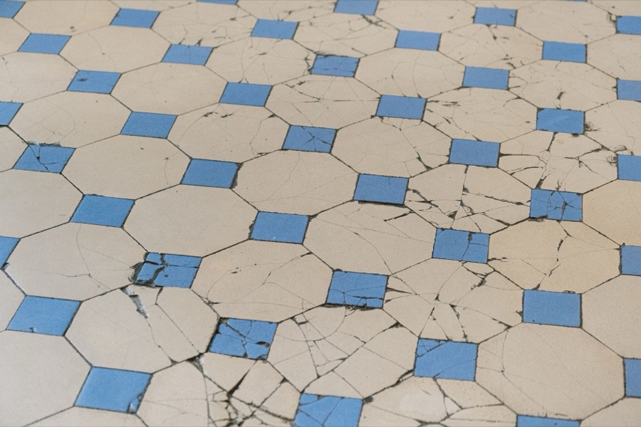 Person's hands using a grout saw to remove old, cracked grout from between floor tiles.