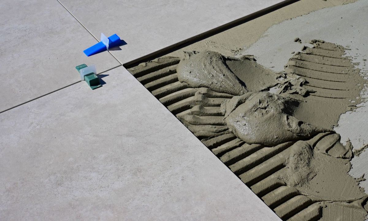 Close-up view of cracked grout lines between light-colored ceramic floor tiles, showing deterioration.
