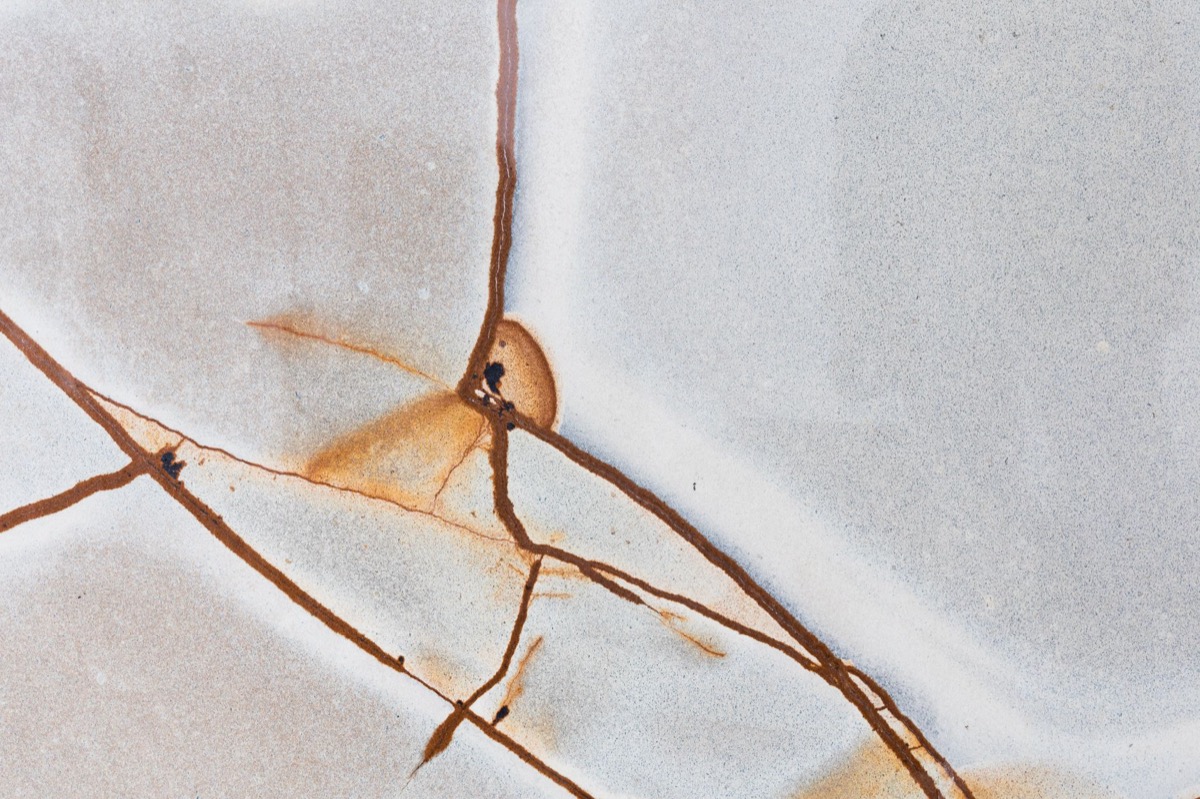 Close-up view of cracked and deteriorating grout lines between white tiles in a shower, indicating damage.
