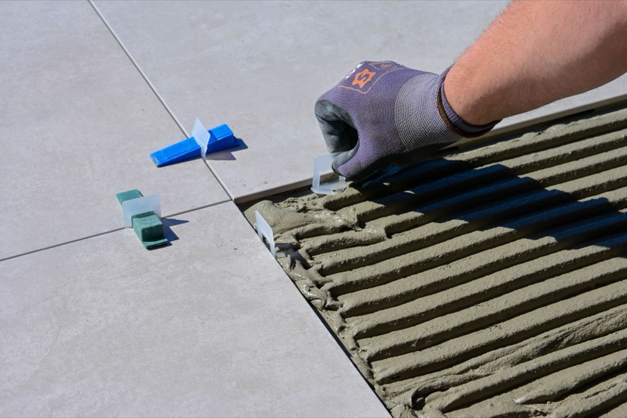 Professional using a specialized digital lippage indicator tool to check for height differences between adjacent floor tiles.