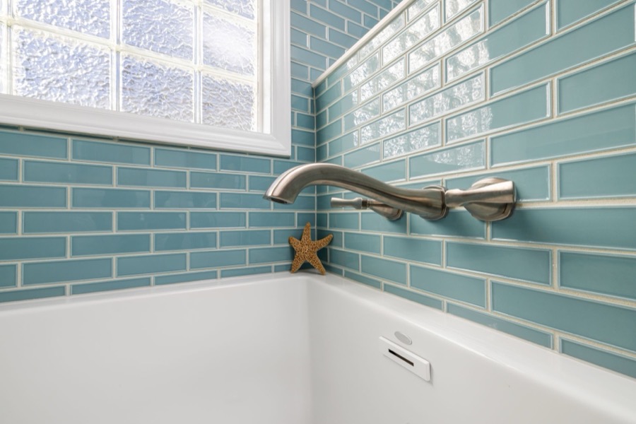 Close-up of a person using a rubber grout float to spread fresh gray grout into the joints of newly installed white subway tiles on a wall.
