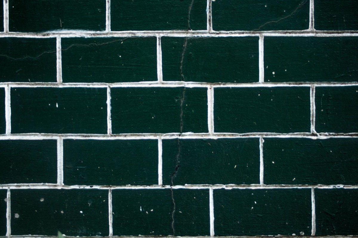 Close-up view of a cracked grout line between white subway tiles in a shower wall, indicating damage.