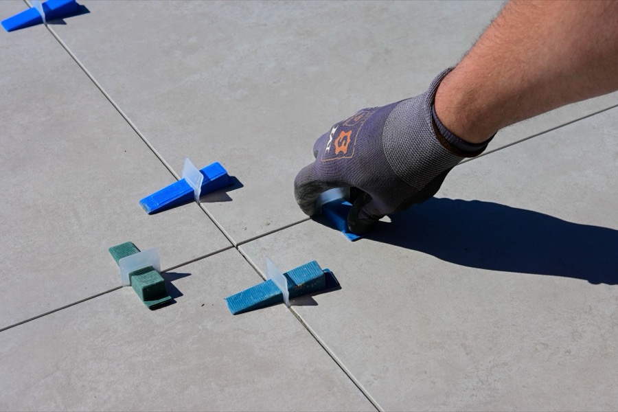 Tile installer using a tile leveling system with wedges and clips to ensure a perfectly flat and even surface during floor tile installation.