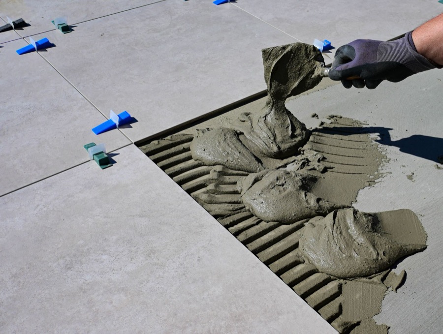 A construction professional inspecting a hairline crack in floor tile grout with a flashlight.